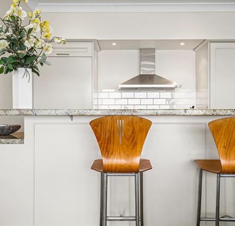 a kitchen with three bar stools and a vase of flowers at Auckland Waterfront Serviced Apartments on Prince's Wharf in Auckland
