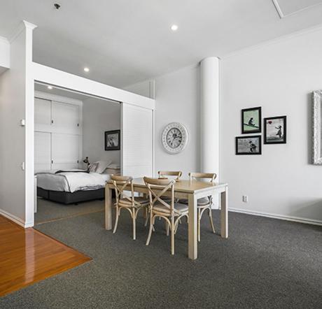 a dining room with a table and chairs and a bed at Auckland Waterfront Serviced Apartments on Prince's Wharf in Auckland