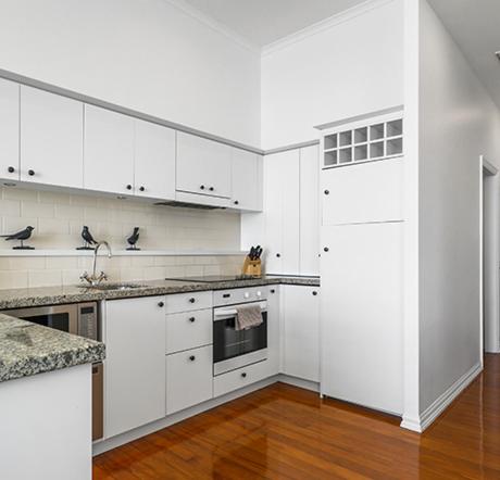 a white kitchen with white cabinets and a wooden floor at Auckland Waterfront Serviced Apartments on Prince's Wharf in Auckland