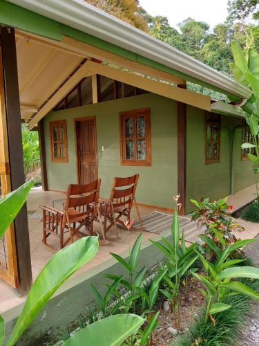 a green house with two chairs and a porch at Cabina Rancho la Merced in Uvita