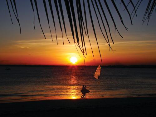 a person walking on the beach at sunset with a sailboat at Serrambi Resort in Porto De Galinhas