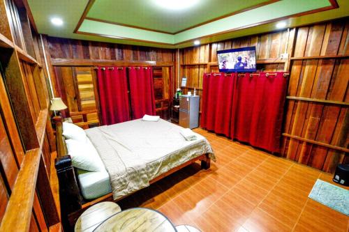a bedroom with red curtains and a bed and a tv at MRK Resort & Massage in Lop Buri
