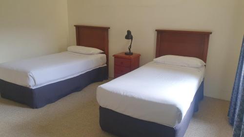 a bedroom with two beds and a lamp on a night stand at Hotel Cavalier in Wantirna South
