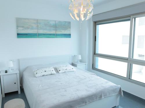 Habitación blanca con cama y lámpara de araña. en Mar Azul 378 Manga Norte, en Murcia