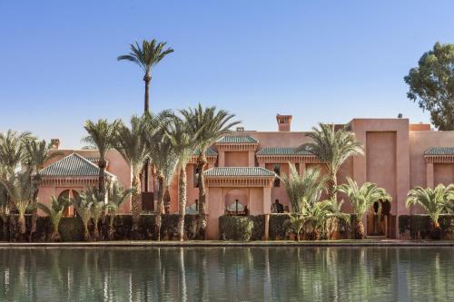 a large pink building with palm trees and a pond at Amanjena Resort in Marrakech