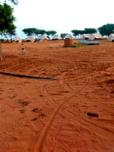 a dirt field with a group of tents in the background at Vamoose Shri Ram Wild Desert Resort in Bikaner