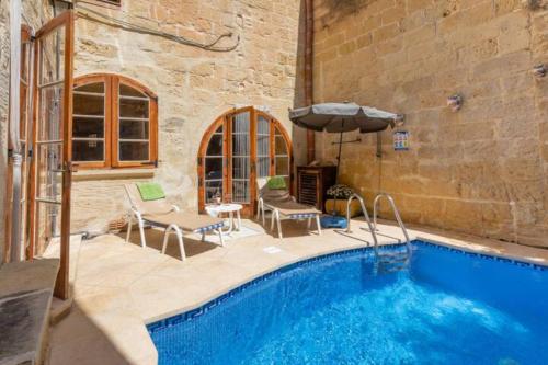 a pool with chairs and an umbrella next to a building at Ta' Frenc Farmhouse in Għarb