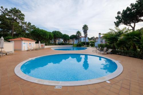 two large swimming pools in a yard with chairs and trees at Maravilhoso T1 Praia D'el Rey in Amoreira