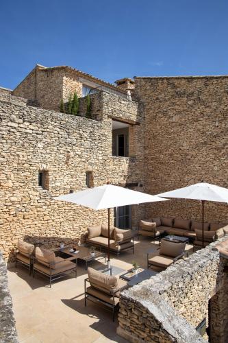 a patio with chairs and umbrellas in front of a brick wall at Mas des Herbes Blanches Hôtel & Spa – Relais & Châteaux in Joucas