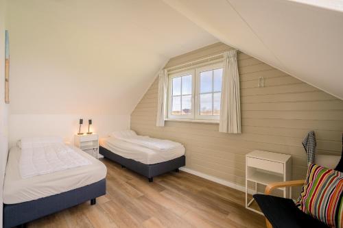 Un dormitorio abuhardillado con dos camas y una ventana. en Annabella 11, en De Koog