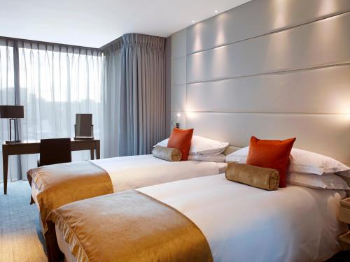 two beds in a hotel room with a desk at Cheval Three Quays at The Tower of London in London