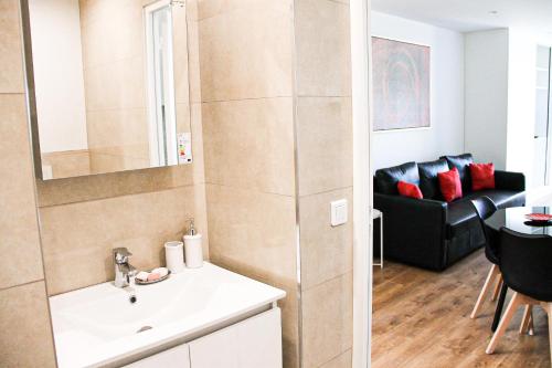 ein Badezimmer mit einem Waschbecken und ein Wohnzimmer mit einem Sofa in der Unterkunft Grand T1 Moderne Jardin près de CDG in Le Thillay