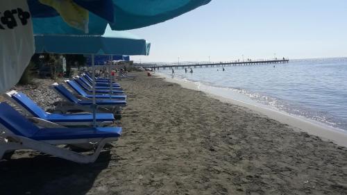 a row of blue lounge chairs on a beach with a pier at Artemis Boutique Apartment 2 in Limassol