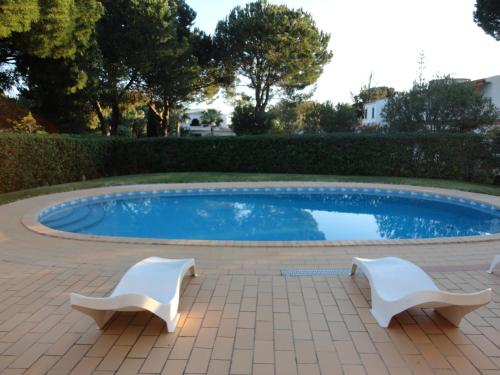 a swimming pool with two white chairs next to it at Villa Cavaco in Vilamoura