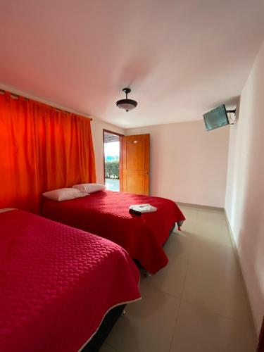 two beds in a room with red sheets and a window at Hotel Las Palmeras Gachancipa in Gachancipá