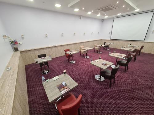 a conference room with tables and chairs and a screen at Kegworth Hotel & Conference Centre in Castle Donington