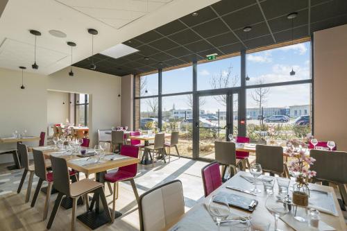 a restaurant with tables and chairs and large windows at Campanile Chartres in Chartres