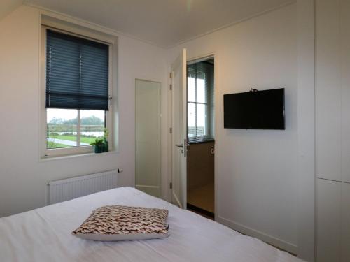 1 dormitorio con 1 cama y TV de pantalla plana en Thatched villa with lounge set, right at the water, en Delfstrahuizen