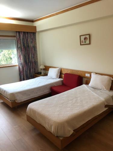Cette chambre d'hôtel comprend deux lits et un fauteuil rouge. dans l'établissement HOTEL CRUZ DA MATA, à Mangualde
