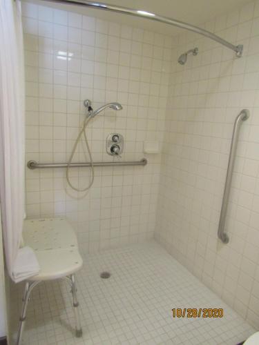 a white tiled shower with a chair in a bathroom at Clarion Inn Near China Lake Naval Station in Ridgecrest