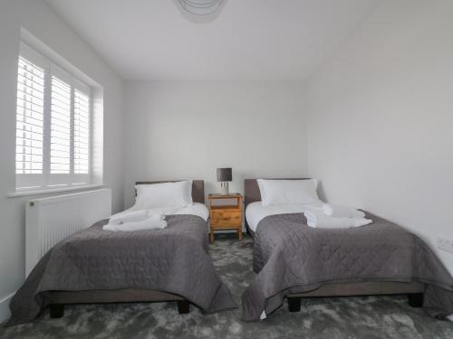 two twin beds in a white room with a window at The Sand Dunes in Crantock