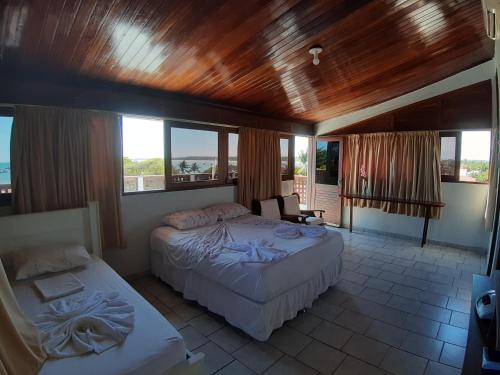 a bedroom with two beds and a balcony with windows at Pousada Mirante do Pontal in Coruripe
