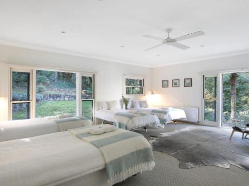 a white bedroom with four beds and windows at The Gullies Retreat in Bundanoon