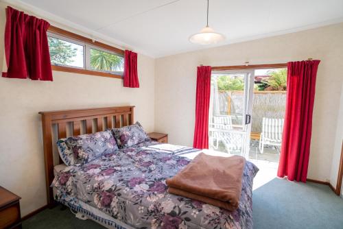 a bedroom with a bed and windows with red curtains at Dee's on Bligh - Te Anau Holiday Home in Te Anau