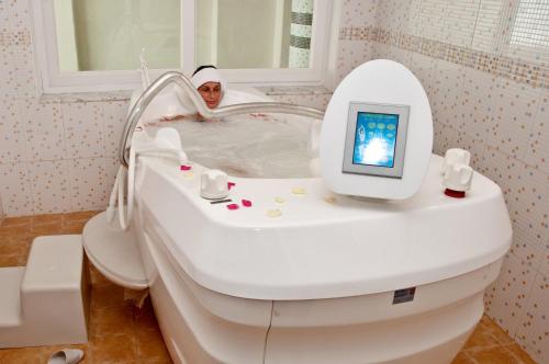 Una suora seduta nella vasca da bagno con una TV sopra di Le Monaco Hôtel & Thalasso a Sousse