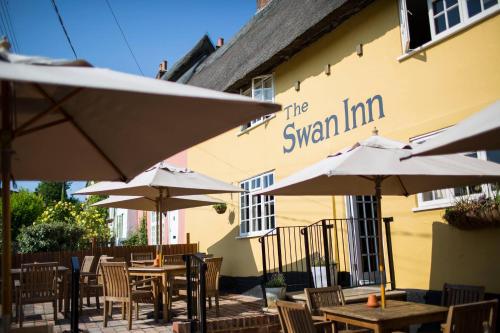 a restaurant with tables and umbrellas in front of a building at The Swan Inn in Monks Eleigh