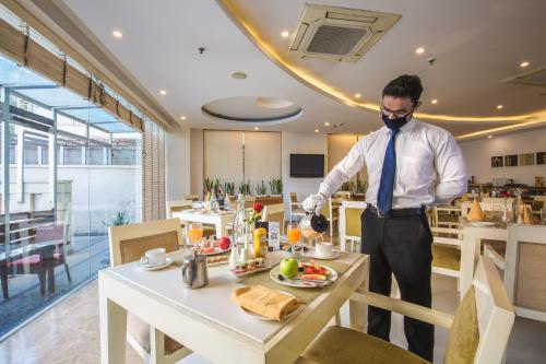 a man wearing a mask and a tie preparing food at Rosewood Apartment Hotel, Gurgaon in Gurgaon