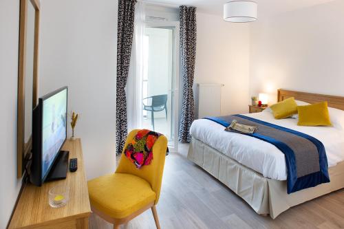 a bedroom with a bed and a tv and a chair at DOMITYS - Olympe in Marcq-en-Baroeul