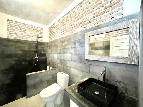 a bathroom with a white toilet and a brick wall at The Breezy Volcano in Kintamani