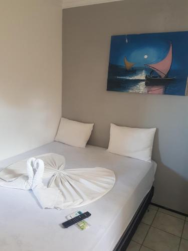 a bed with white sheets and a picture on the wall at Pousada Veleiro in Fortaleza
