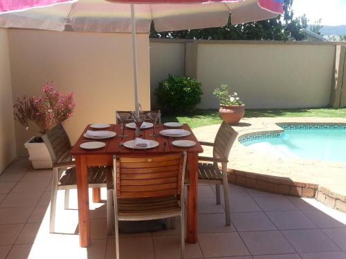 a wooden table with chairs and an umbrella next to a pool at Majestic in Kokstad