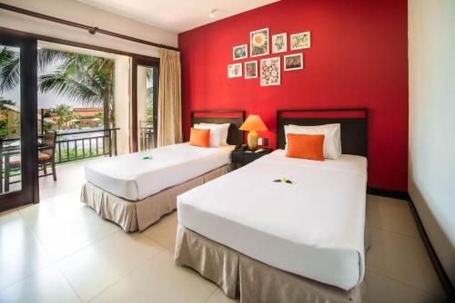 two beds in a room with a red wall at Pandanus Resort in Mui Ne