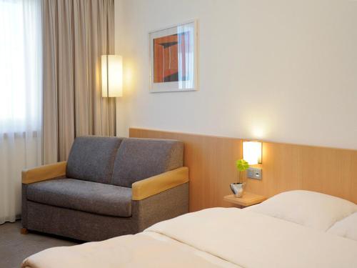 a hotel room with a chair and a bed at Novotel Düsseldorf City West in Düsseldorf