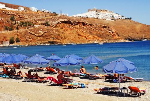 a group of people sitting on a beach with blue umbrellas at Astropalia Luxury Studios in Astypalaia Town
