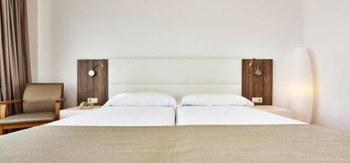 a bedroom with a large white bed and a chair at Globales Cala Viñas Adults Only 16+ in Cala Vinyes