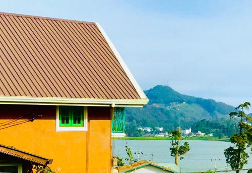 ヌワラエリヤにあるSerendipity Lake Artistic Bungalow by Heidis Homeの水面の見えるオレンジ色の建物