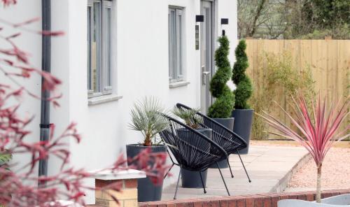 a patio with two black chairs and potted plants at Pen-Y-Worlod Cottages in Abergavenny