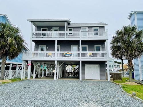 a large white house with a balcony and palm trees at Beach Bells Home in Holden Beach