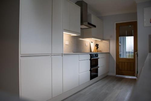 una cocina con armarios blancos y una puerta en Large family Bungalow, parking & Bike Store BPW, en Merthyr Tydfil