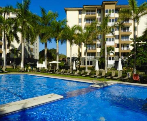 Una piscina con palmeras y un edificio. en Condominios Costa Linda, en Jacó