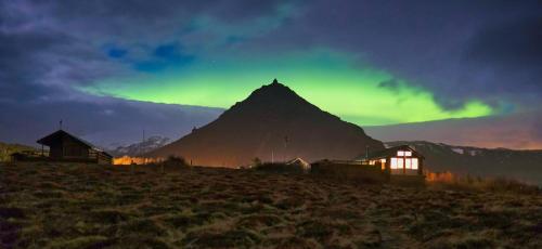 a mountain with a green sky and some buildings at Lava House on the Ocean in Arnarstapi