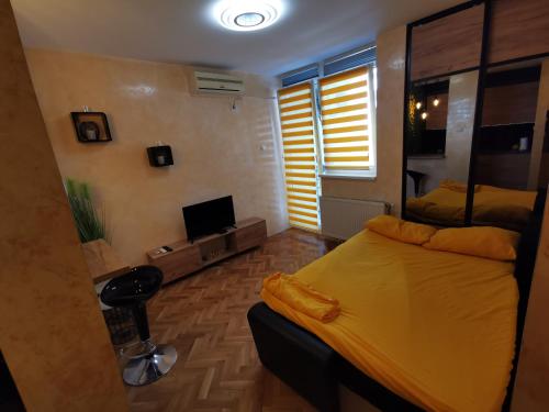 a bedroom with a yellow bed and a television at Centar Stan na dan sa besplatnim parkingom in Novi Sad