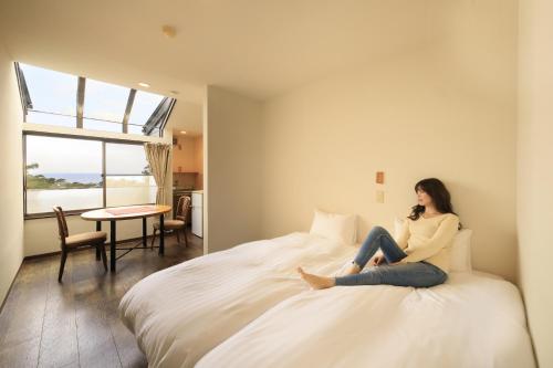 下田市にあるWelcome Inn SunnyStepsの携帯電話で話しながらベッドに座っている女性