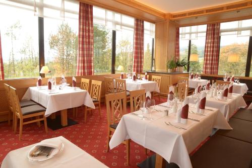 um restaurante com mesas e cadeiras brancas e janelas em Hotel Kaiseralm em Bischofsgrün