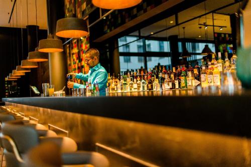 a man standing at a bar with a drink at Motel One Köln-Neumarkt in Cologne