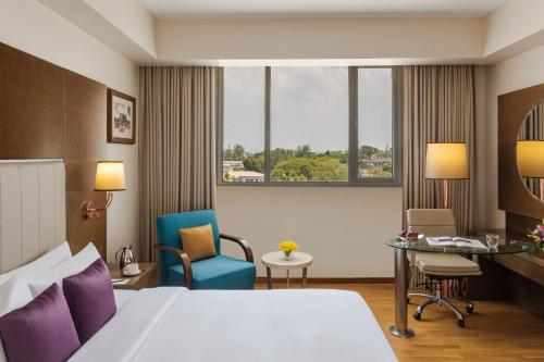 a hotel room with a bed and a desk and chairs at Vivanta Thiruvananthapuram in Trivandrum
